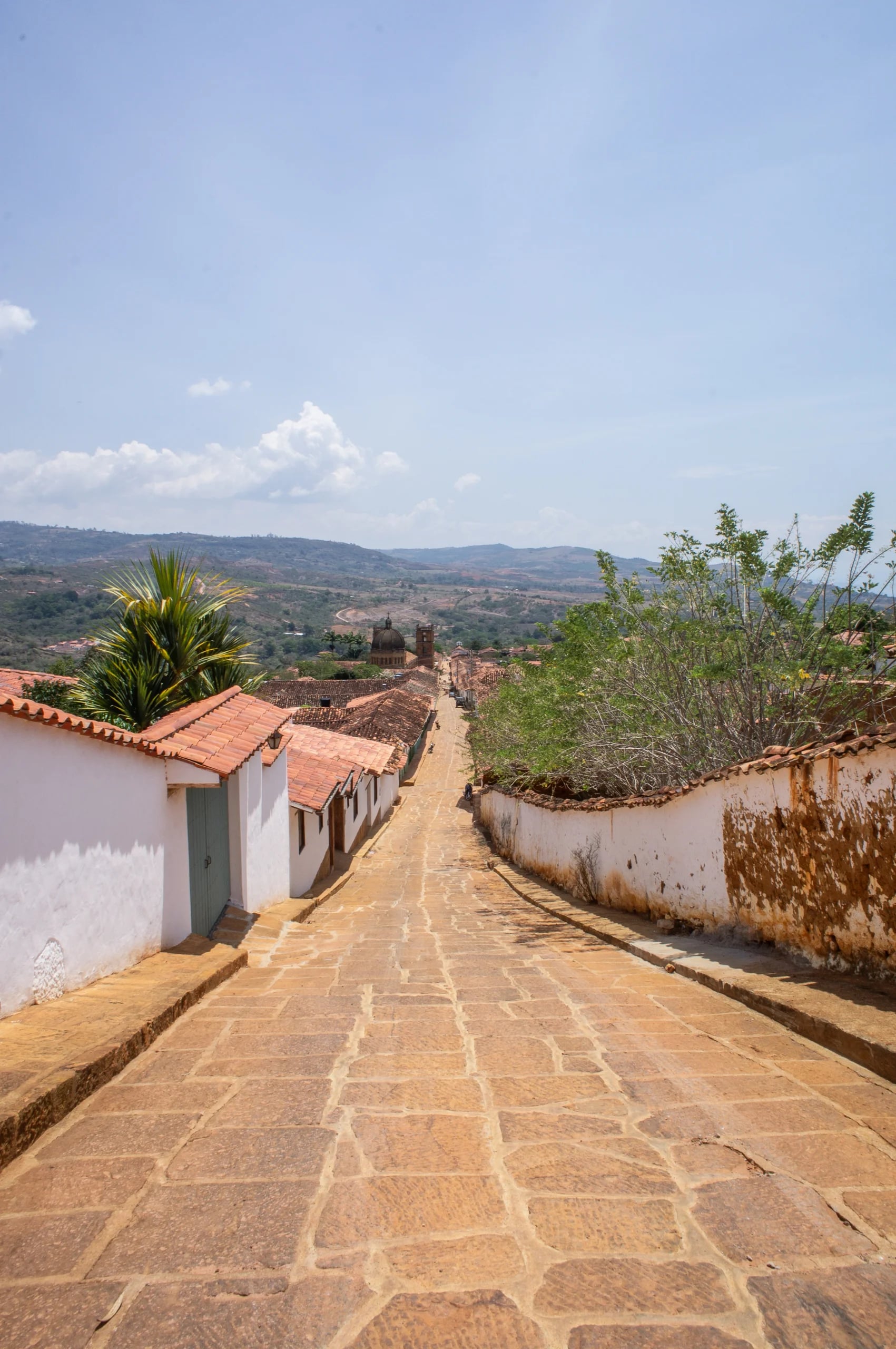 A stone-paved street dropping away between whitewashed houses in Barichara, hills folding into the distance
