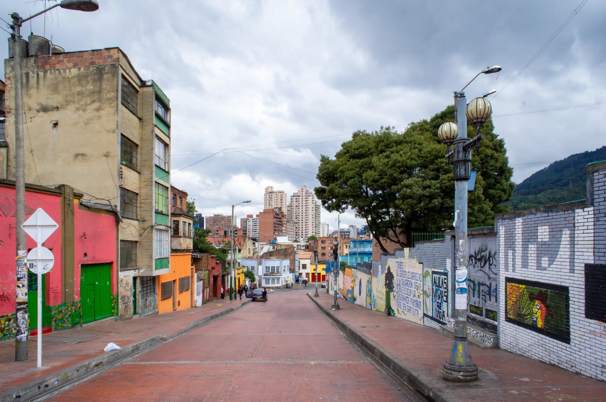 An empty brick street running downhill through La Candelaria, graffiti along one wall and the city towers beyond