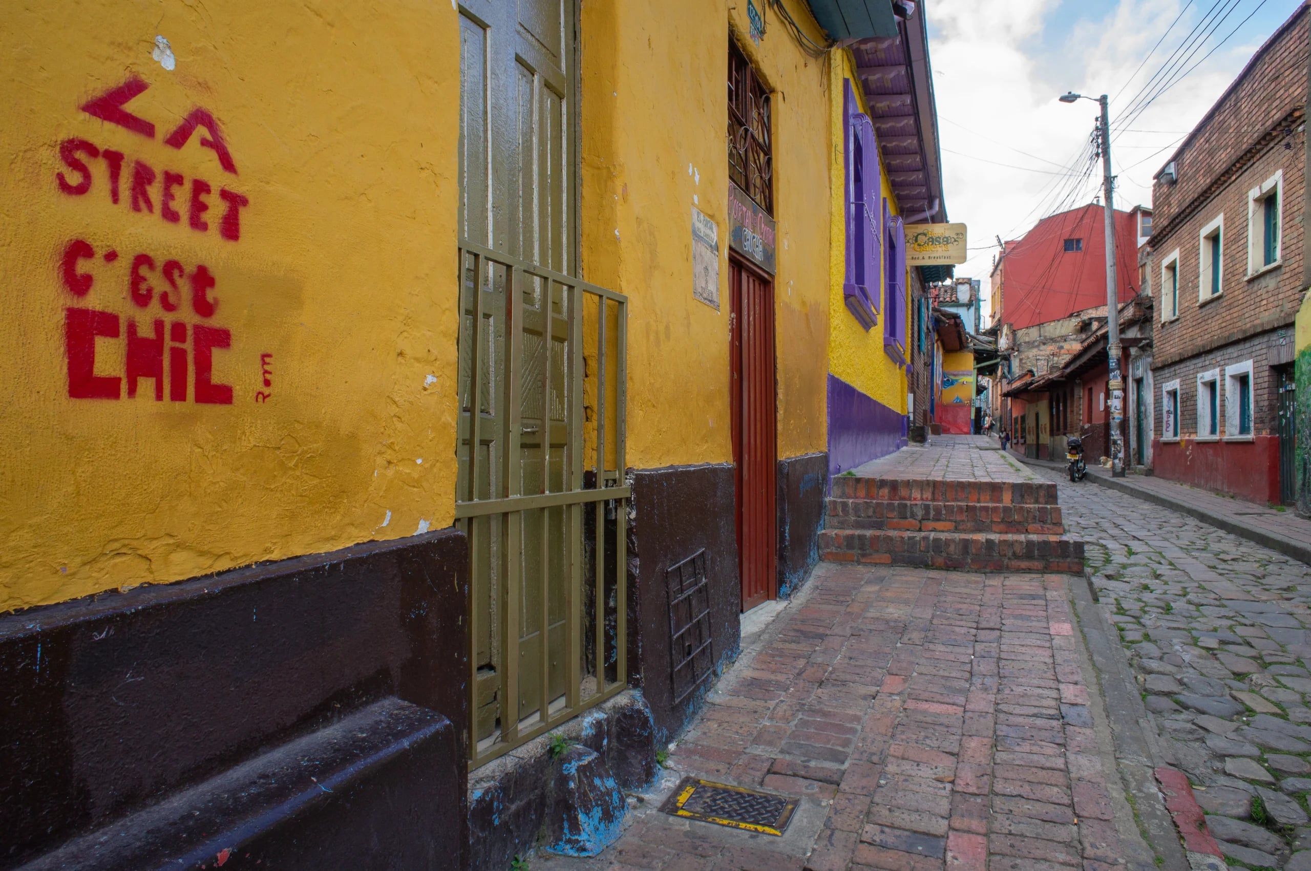 A cobbled lane climbing between ochre and purple walls, LA STREET C'EST CHIC painted in red on the corner