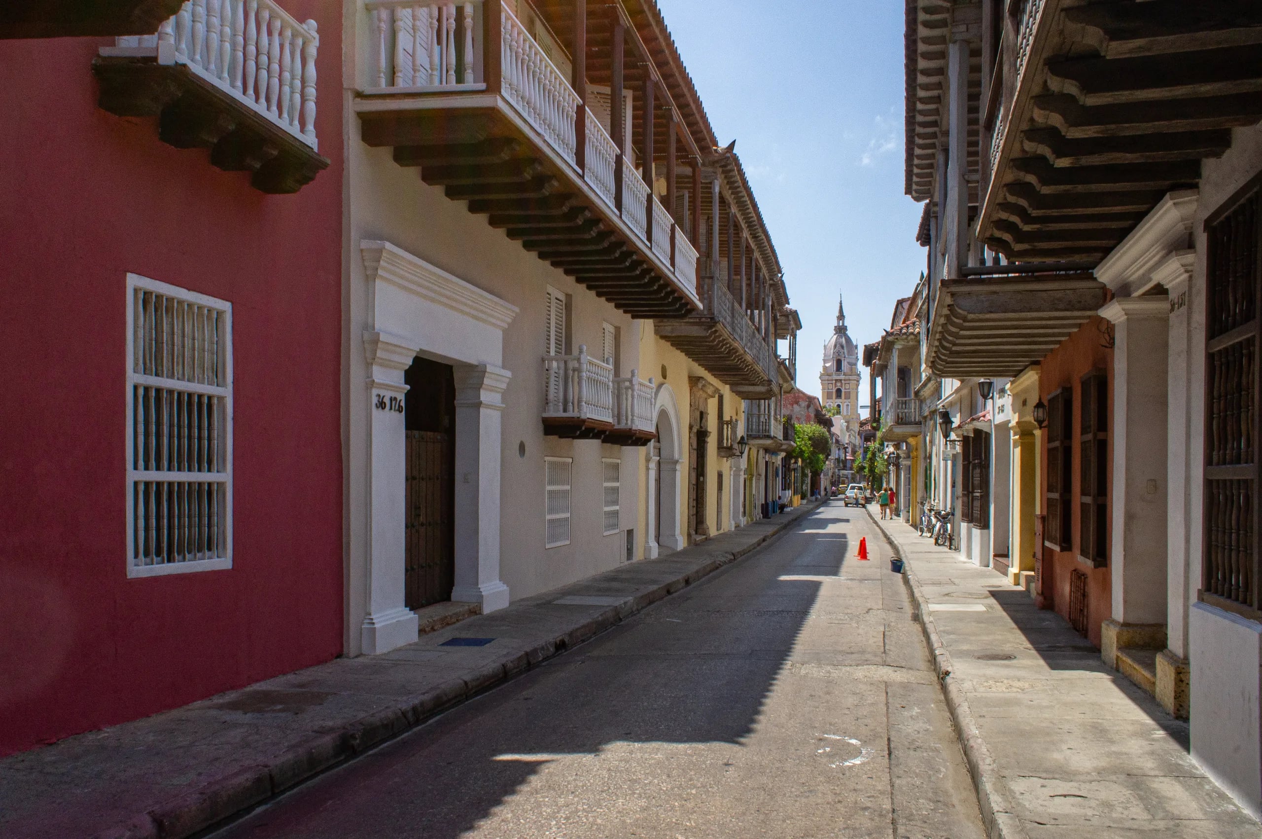 A narrow street in the walled city, wooden balconies overhanging from both sides and a deep red house in the foreground, with a church tower closing the view at the far end.