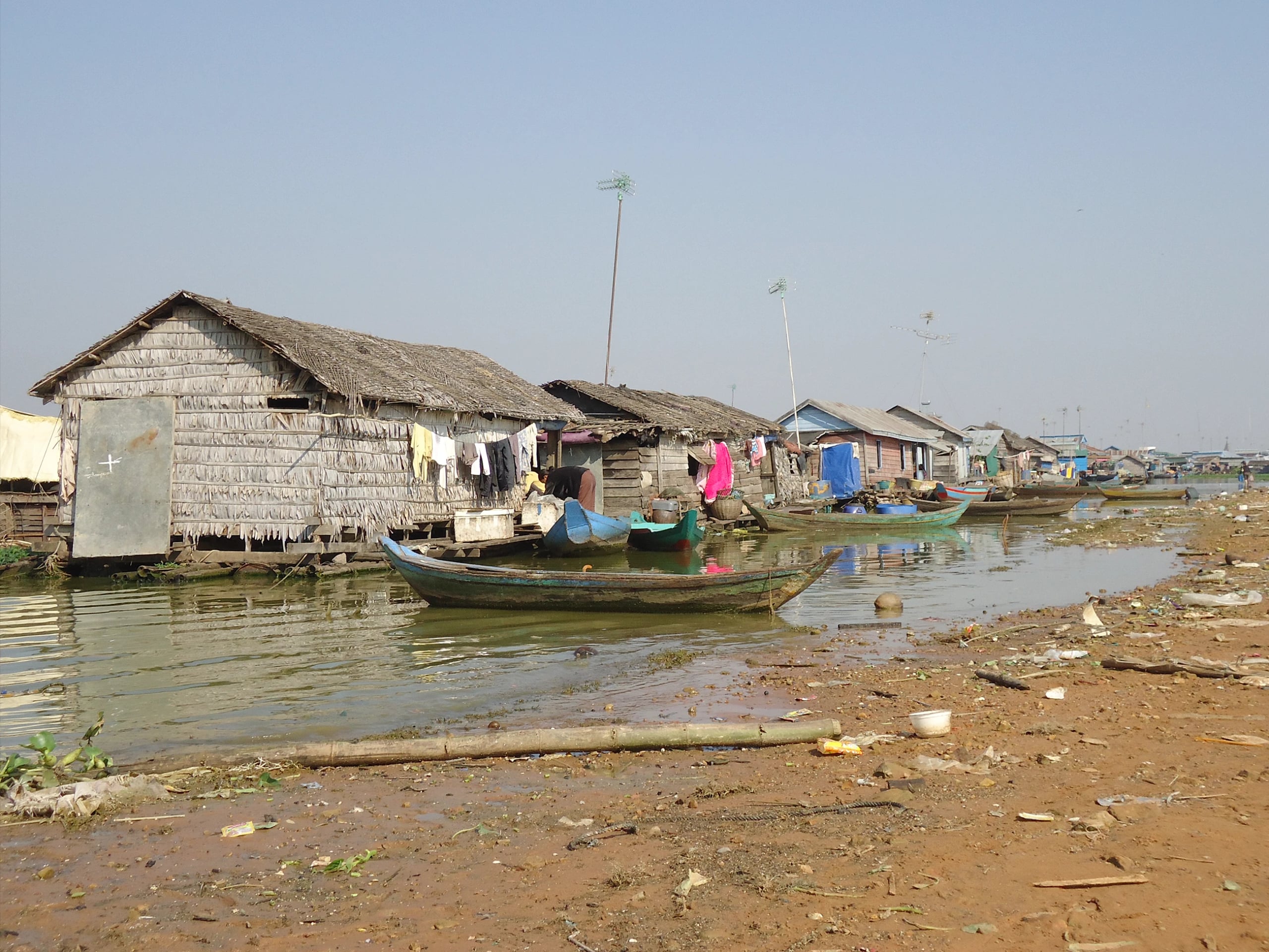 Thatched stilt houses along a muddy shoreline, wooden boats drawn up and laundry hung out to dry