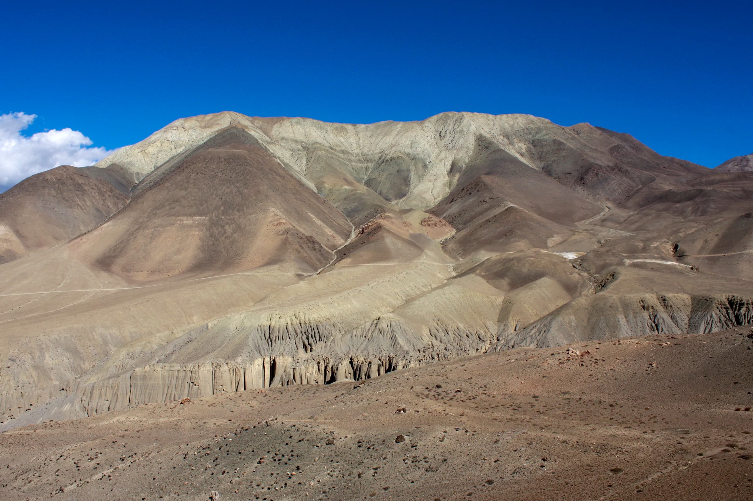 Bare, treeless mountains in brown and pale green under a deep blue sky, their lower slopes cut into fluted columns by erosion.