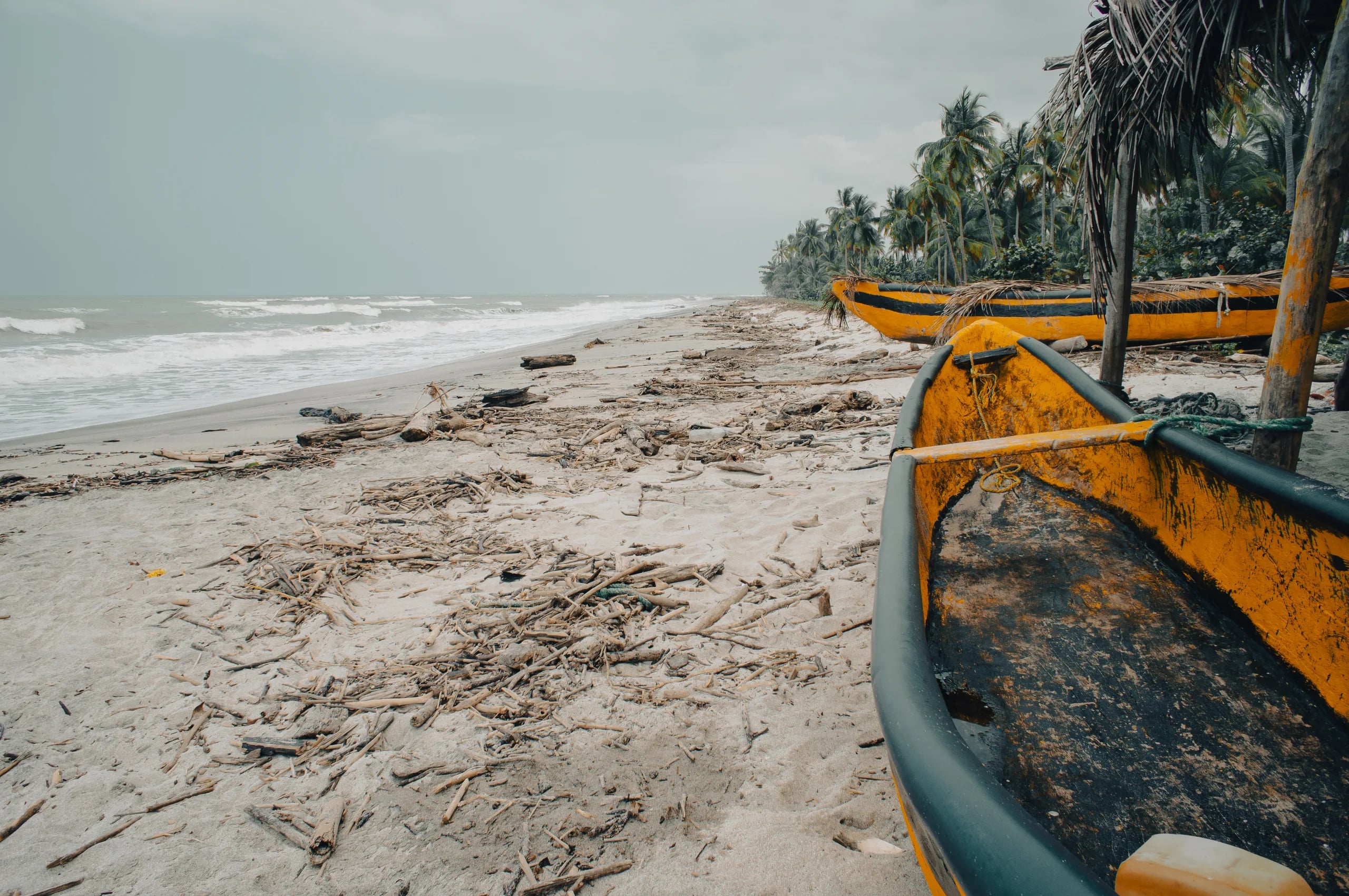 A yellow fishing canoe drawn up on the sand, driftwood and debris scattered along the tideline