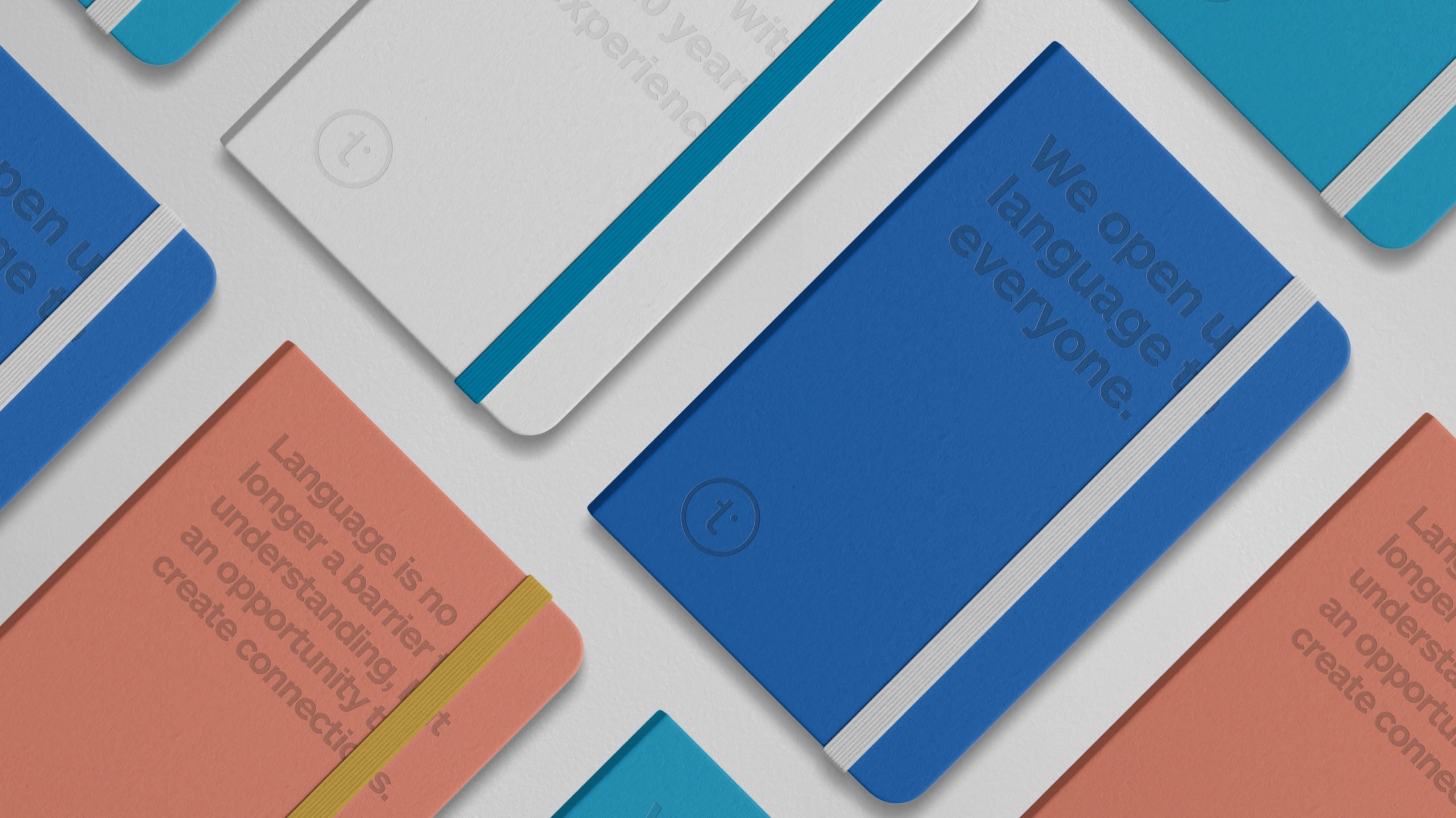 Branded notebooks laid out at an angle in blue, coral, cyan and grey, carrying the t mark and brand lines such as We open up language to everyone